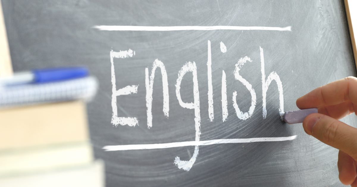 Hand writing on a blackboard in a language class with the word "English" wrote on. Some books and school materials.